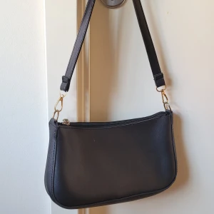 Svart axelremsväska - Svart axelremsväsla. Inga tecken på användning. Perfekt storlek; telefon, nycklar, airpods, läppglans, allt får plats och mycket mer🥰. Säljer då den inte används lika mycket som jag hoppades på🤗. 