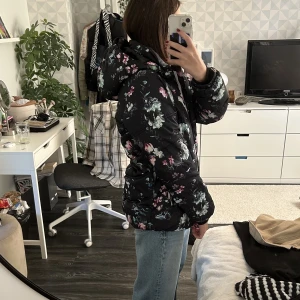 Vinterjacka  - Säljer min tjocka dunjacka ifrån märket ”Warp” den är svart med rosa/gröna/blåa blommor och blad på, den är i väldigt bra skick i storlek 158/164. Nästan aldrig använts. Originalpris 699