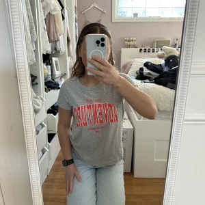 Grå t-shirt med text - En t-shirt med orange text från Ginatricot