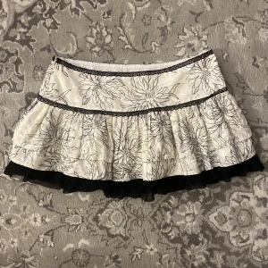 Volangkjol med blommor - Vit och svart volangkjol med blommigt mönster🤍Den har en dragkedja på sidan!