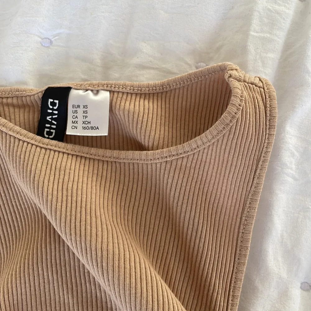 Ett beige linne från H&M, divided. Har inte kommit till användning. Små knyte på sidan där man kan spänna åt hur mycket man vill ha den cropad!!😍(ser litet ut men är jätte ”töjbar”). Toppar.