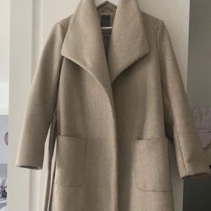 Beige kappa - Beige kappa från Primark. Storlek 38. Något nopprig men skön modell. Fickor fram samt knytning.