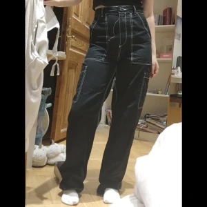 Svarta cargo pants - Ett par svarta jeans i cargo aktig modell med vita detaljer. Storlek 34 men passar bra på mig som brukar ha S. Använda några gånger men fortfarande i mycket bra skick. Köpta från h&m.