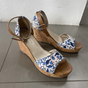 Blommiga sandaler med kilklack - Snygga sandaletter med kilklack i mycket bra skick. Använda 1 gång. Klackhöjd 8cm, köpta från Din Sko. Normal i storleken.