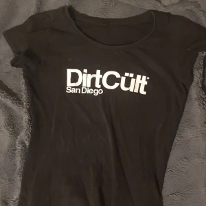 Svart Dirtcült tshirt - En svart dirtcült tshirt, lite slitage på loggan annars i bra skick (ignorera katt håret) säljer den eftersom den inte är min stil längre, är en XS men passar S lika bra💕