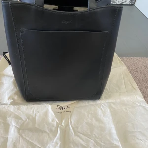 Filippa K shelby mini bucket bag - Svart väska från Filippa K, Shelby Mini Bucket Bag. Använd ett fåtal gånger.  Väskan har axelrem och dubbla handtag. Väskan har ett stort huvudfack som stängs med magnet, ett mindre fack på sidan samt ett litet innerfack med dragkedja.  Mått: 20x20,5x16 c