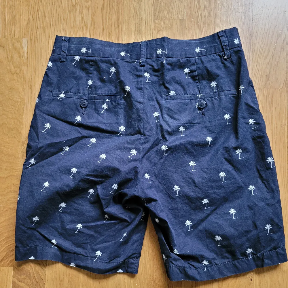 Blå shorts med palmer på. Fickor fram och bak. Tyget har bleknat lite på vissa ställen, syns på sista bilden. . Shorts.