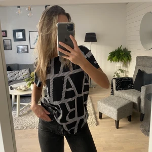 Svart glansig t-shirt  - Glansig t-shirt med tryck som påminner om siden utseende mässigt. Ingen stretch men ändå väldigt skön. Använd ett fåtal gånger men är nästan som ny.