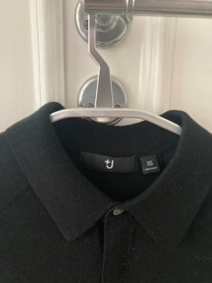 Kragtröja Jil Sander x Uniqlo - Svart kragtröja från Uniqlo med knappar i ullblandning. Tröjan är är knappt använd och i gott skick. Storlek XS (herr)