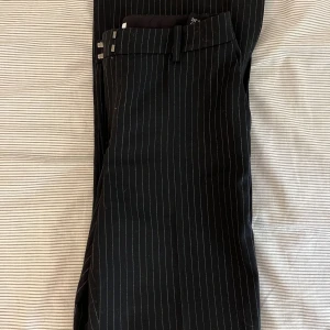 Kostymbyxor randiga med flare leg m slits - Dessa fina kostymbyxor från other stories är sitter så smickrande men är tyvärr försmå. De har dragkedja och Även en knapp och två hakar vilket gör att se sitter smickrande över magen. Finns även slits vid fötterna. OBS INNERTYGET ÄR SVART!!