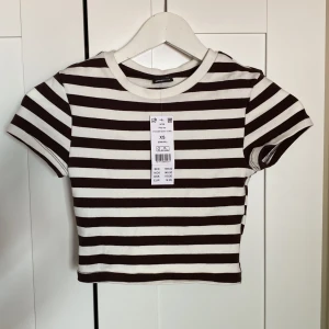 Brunrandig T-shirt  - Brun och vitrandiga T-shirt från ginatricot, aldrig använd med lappar kvar! Stretchiga och skön. Croppad 