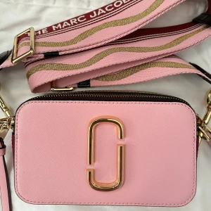 Marc Jacobs - Snapshot rosa  - Äkta Marc Jacobs väska köpt från Johnells för 3 699. Inte kommit till användning och vill därför sälja den så fort som möjligt. Väskan är i vädligt bra skick och har inga fel. Tillkommer med dustbagen som jag fick med. Pris går att diskutera! 