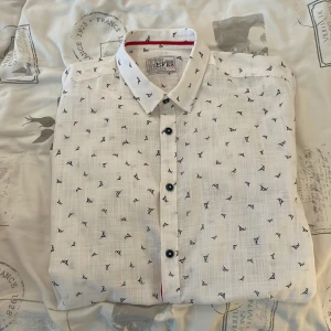 Vit skjorta  - En vit skjorta från selcuk efes. Skjortan har ett mönster av svärdfiskar. Den är i storlek large. Hör av dig för fler bilder eller frågor.