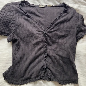 Söt Levis topp - Grå/svart tröja med små knappar i mitten och volang runt hela tröjan! Storlek M men passar S och kanske Xs för den är rätt liten men stretchig! Fint mönster på hela tröjan som gör att den ser lite mer speciell ut! 