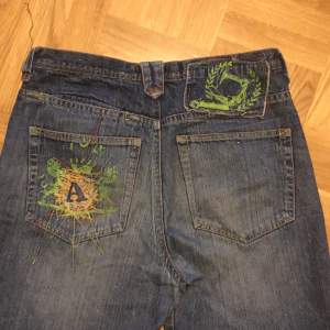 Vintage baggy jeans med en cool detalj på fickan! Söndriga längst ner därav priset🤝 Midjemått: 86cm Längd: 102 cm