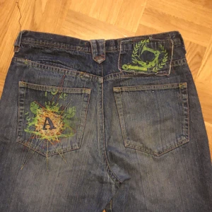 Baggy jeans - Vintage baggy jeans med en cool detalj på fickan! Söndriga längst ner därav priset🤝 Midjemått: 86cm Längd: 102 cm