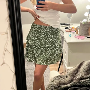 Grön kjol med vita blommor - Grön kort kjol med volanger och vita blommor från Vero moda. Strl M.