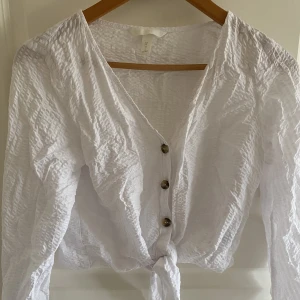 Vit topp med knytning - Croppad vit topp från H&M som kan knytas och knäppas eller lämnas öppen. Toppen är i tunt material vilket gör den bra inför sommaren