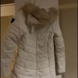 En vit vinterjacka och grå inne i jackan luva med päls