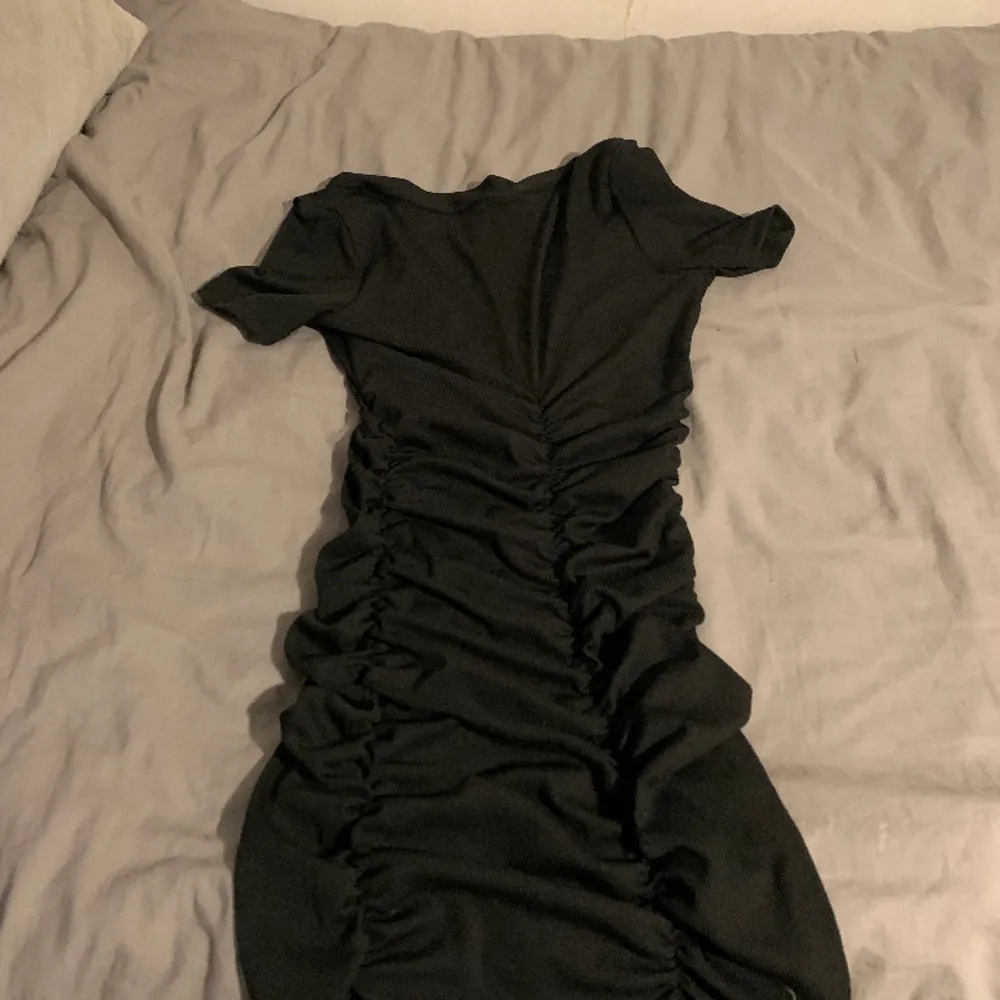 En klänning som är svart med knapar på som inte kan knappa upp det är  det är en  Stretch klänning som är V-ringad vi brösten storlek XS kan stretcha ut till storlek medium❤️ står inte var den kommer ifrån. Klänningar.