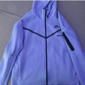 Helt Ny Lila Nike Tech - Hej där! Jag säljer en helt ny lila Nike Tech-tröja som kommer att ge din stil en uppgradering! Denna tröja är inte bara snygg utan också bekväm, perfekt för både vardag och träning.   