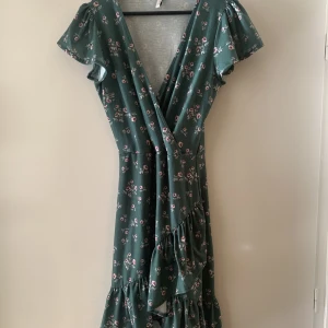 Grön & blommig omlottsklänning - Vääärldens sötaste rosablommiga omlottsklänning i en fin grön färg. Storlek XS men skulle säga att den är ganska stor i storleken 🥰