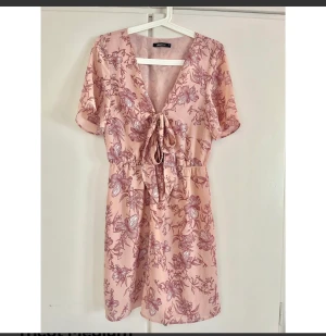 Rosa klänning Gina Tricot Medium  - Blommig klänning med urringning. Urringningen knyts med en rosett, vilket är en snygg detalj! Går ungefär ner till ovanför knäna.