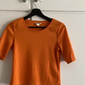 Orange croppad t-shirt i storlek S.  Lätt glansig finish!  Smalribbat tyg Knappt använd, nyskick! 