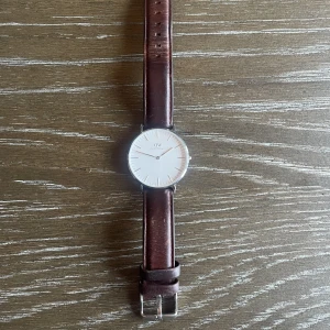 Daniel Wellington klocka!  - En silvrig Daniel Wellington klocka med brunt armband. Är i fint skick, dock behöver batteriet bytas ut. 