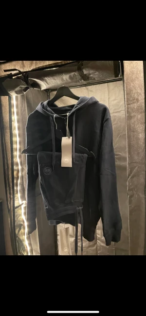 Canada goose - Splitter NY navy blue tracksuit från Canada Goose. Tillverkad av 100% bomull. Justerbar luva med dragsko, ribbstickad fåll och ärmslut och två handfickor framtill. Rund patch med logtoyp på vänster ärm. Samt Patch på vänsta sidan  På byxan 
