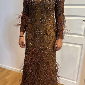 Festklänning  - En unik festklänning i brun färg med stenar & fjädrar. Klänningen är inköpt i Frankfurt i butik för 400€   Använd en kväll och är i nyskick.   Passar storlek S/36 