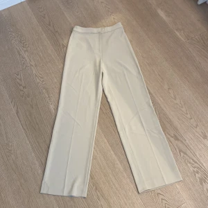 Kostymbyxa  - Högmidjad kostymbyxa i ljusbeige. Strlk 34 men töjer sig något så passar även en 36a. 
