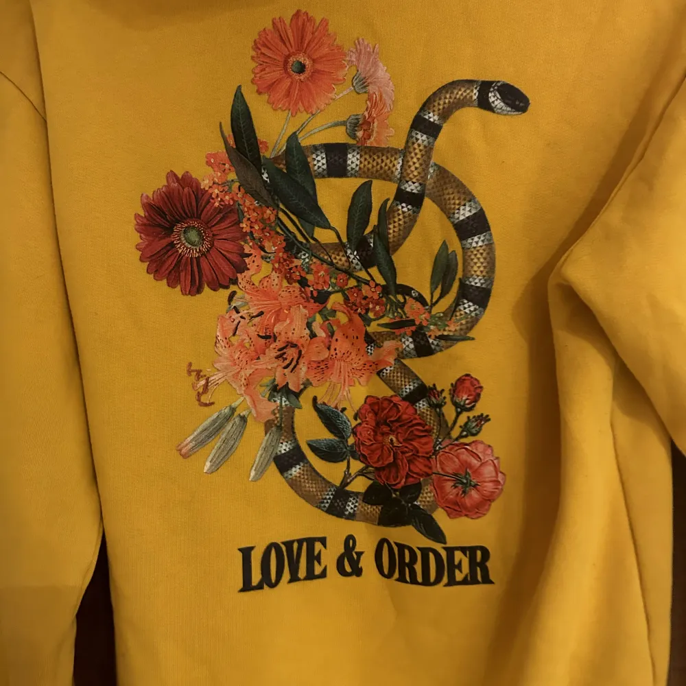 En gul/orange jätte fin hoodie med text ”love and order” och som har ett coolt tryck på ryggen!. Hoodies.