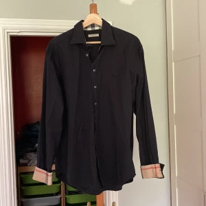 Burrbery skjorta, svart, XL - Jag säljer min Burberry skjorta i fint sick. Den är tidigare köpt på plick och säljs därför den visade sig vara för stor. Stilren utan fläckar eller missade tillbehör!  