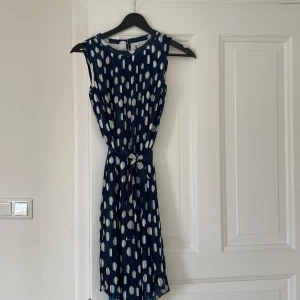 Finklänning marinblå med vita prickar  - Somrig finklänning (eller cocktailklänning) i marinblått med vita prickar. Skirt tyg i två lager, med band att knyta i midjan. Sparsamt använd, på skolavslutning och liknande. 
