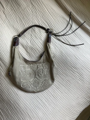 Guess-väska  - Superfin liten axelremsväska från Guess. Den är blekt gröngrå mot det beiga hållet och läderdetaljerna är äkta:)