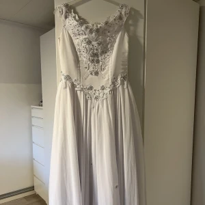Balklänning - Säljer denna fina klänning som är precis som ny. Klänningen är vit med silverstenar. På kjolen är det blommor. Dragkedja i ryggen. Finns även en underkjol och handskar som ingår i priset. Finns inga defekter eller fläckar. Nypris 10 000. Strl M