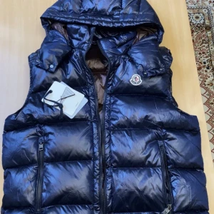 Moncler väst - Helt ny moncler väst med luva. Puff moncler väst med NFC skann, luva, i storlek 3/L och färgen mörkblå. Västen är oanvänd i nyskick. Fin matrial och topp kvalite. Det är definitivt en ”en gångs deal”. Har du några frågor tvivla inte att skriva till mig :)