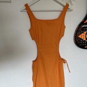Jättefin orange långklänning som aldrig har använts, slutar under knäna på mig som är 167cm. Detaljer vid midjan 
