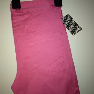 NYA och oanvända byxor. Slim fit / skinny / smala ben. Neonrosa, cerise. Storlek: 32/XS. - Helt nya och oanvända neonrosa/cerisa smala/slim fit byxor. Storlek: 32/XS. Materal:  Bomull. Lappar/tags sitter kvar sedan inköpet. Har fickor fram+bak och hällor för skärp. Helt felfria. Nypris i butik var 198 kr.