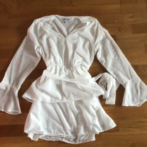 Vit klänning - En vit klänning från Madlady med snörning. Volanger på nedre delen och en volang vid slutet av armen. 