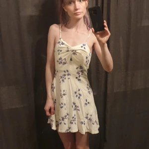 Miniklänning - Vit kortklänning med blommor i lila och blått :) i lite grövre tyg. Nyskick.