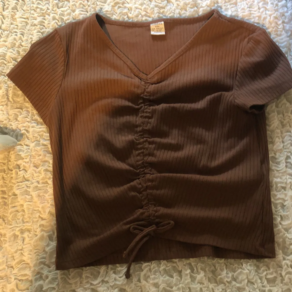 Säljer denna bruna t-shirt från Lindex. Aldrig använt och inga defekter. Som ni ser är det knyte nertill!. Toppar.