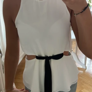 Vit topp med svart band  - Supersnygg topp till 🎊 fester! Har en liten gul fläck i midjan där svarta bandet är men syns inte då bandet är på.