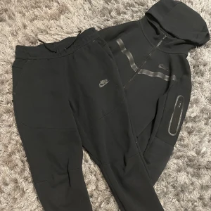 Nike Tech Set - Jag säljer detta Svarta Nike Tech Set som inte kommer till användning. Kan köpas var för sig. Tröjan för 600kr och byxorna för  700kr. Om köp tillsamman 1200. (Pris kan diskuteras) Tröjan är i barn storlek M och byxorna i barn storlek L.