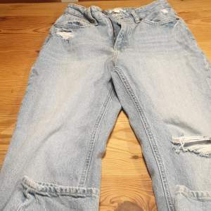 Ett par ljusblåa raka jeans med ett hål på vänstra knäet och ett liten uppe på högra låret. Från HM.