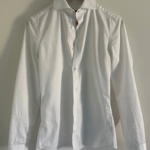 Riley Skjorta Vit  - Fräsch vit skjorta från Riley, köpt hos brothers. Använd ca 3 gånger. Passar precis på dig som är ca 170cm, precis för liten på mig som är 175cm. Finns inga tecken på användning. Perfekt till skolbalen, fester eller bara välklädd till på en varm dag eller utan en tröja. Jag säljer även riktigt snygg kostym i samma storlek till bra pris, av samma märke! Hör av en om ni har några frågor!