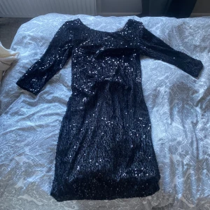 Svart paljettklänning -  svart klänning täckt med glittrande paljetter. Den har trekvartsärmar och ryggen har en ringning, alltså är den pyttelite öppen i ryggen. Går ungefär till knäna. Aldrig använd, köpt för 69 kr men då den inte har några defekter eller tecken på användning säljer jag den till samma pris. Okänt märke 