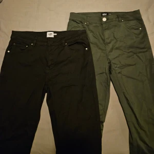 Svarta och gröna byxor från 157 - Två oanvända par byxor från 157, ett par i svart och ett i grönt. Båda har en klassisk femficksdesign med knapp och dragkedja framtill. Perfekta för en avslappnad stil.