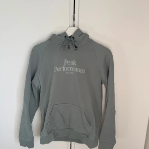 Grå hoodie från Peak Performance - Säljer en stilren grå hoodie från Peak Performance. Tröjan har en klassisk design med en känguruficka och justerbar huva med dragsko. Perfekt för en avslappnad stil.